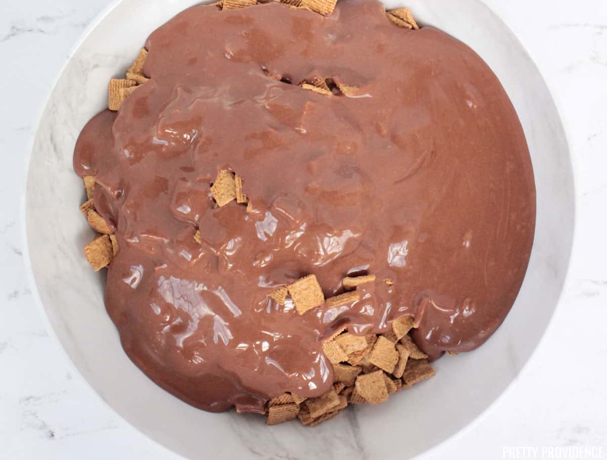 Melted chocolate and marshmallow in a bowl over golden grahams cereal, part of the process for making golden grahams s'mores treats.