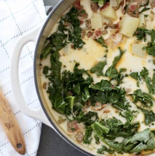 large white pot of Zuppa Toscana soup on a cement counter next to wooden spoon and tea towel