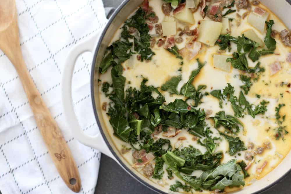 large white pot of Zuppa Toscana soup on a cement counter next to wooden spoon and tea towel