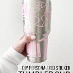 hand in white sweatshirt holding a stainless steel tumbler with pink stickers