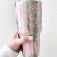 hand holding sticker covered tumbler in front of a white wall