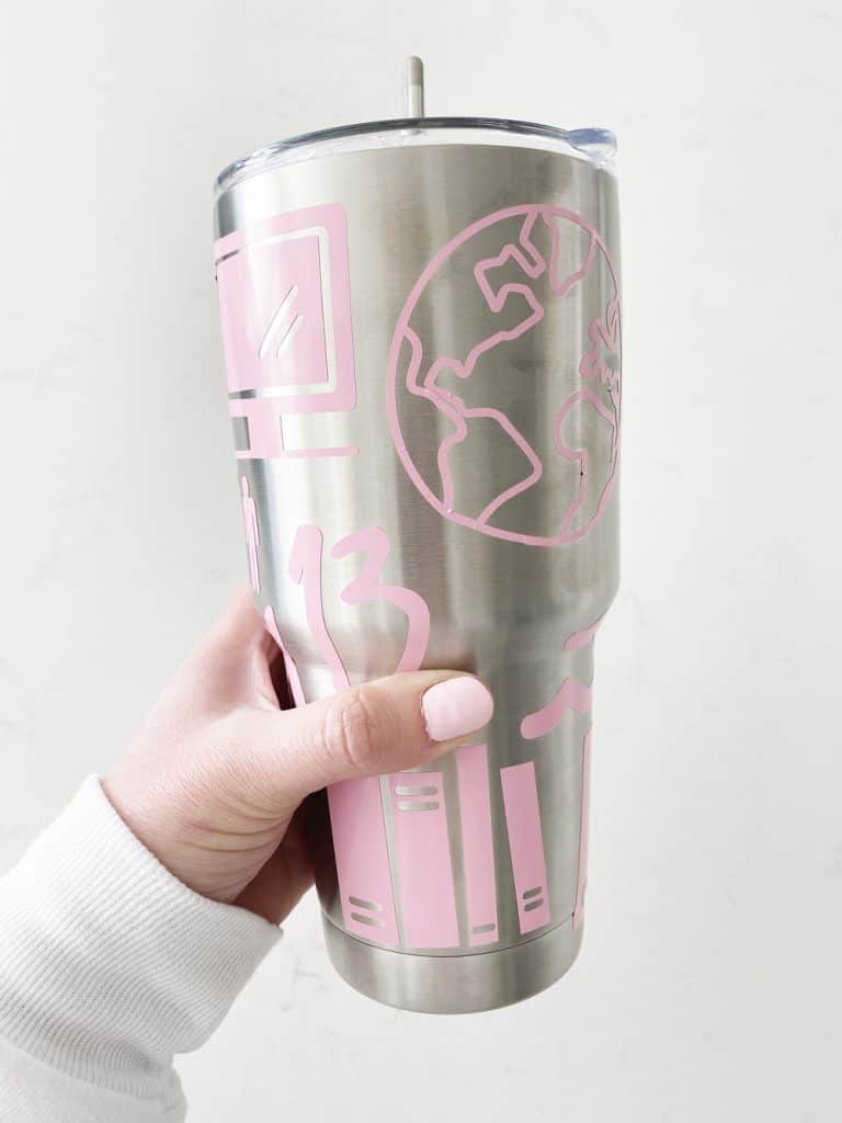 hand holding sticker covered tumbler in front of a white wall