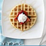 yeast waffle on a white plate with berries and whipped cream