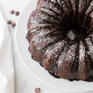 a chocolate bundt cake on a white cake stand on a white countertop