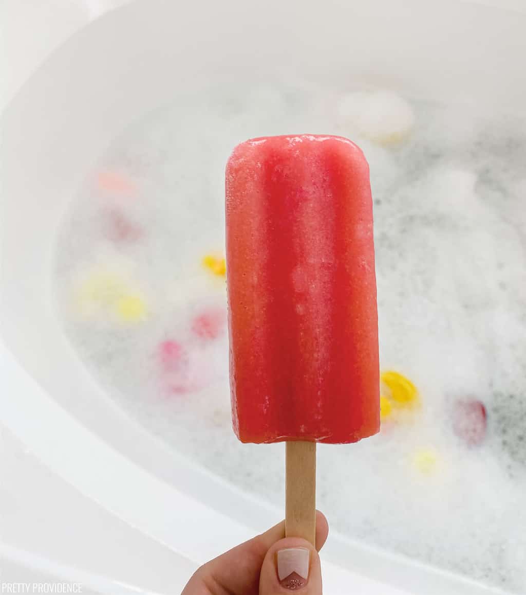Red popsicle being held over a bubble bath - fun kids and toddler activity idea.