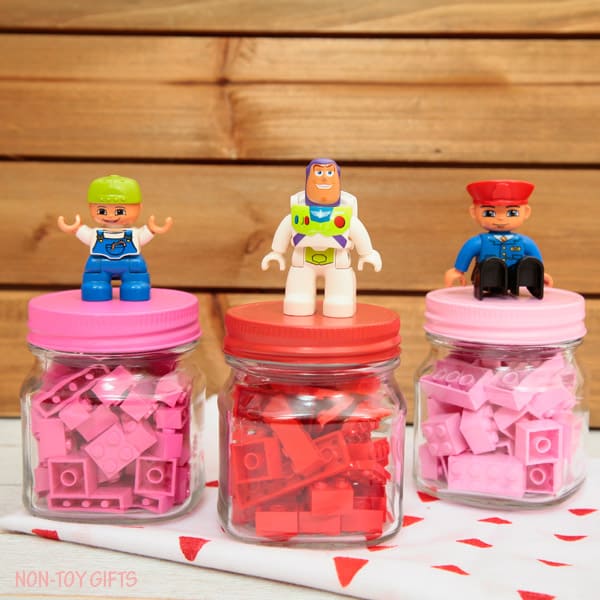 Pink legos and red legos in jars with minifigures glued to the lids - cute toy Valentine idea