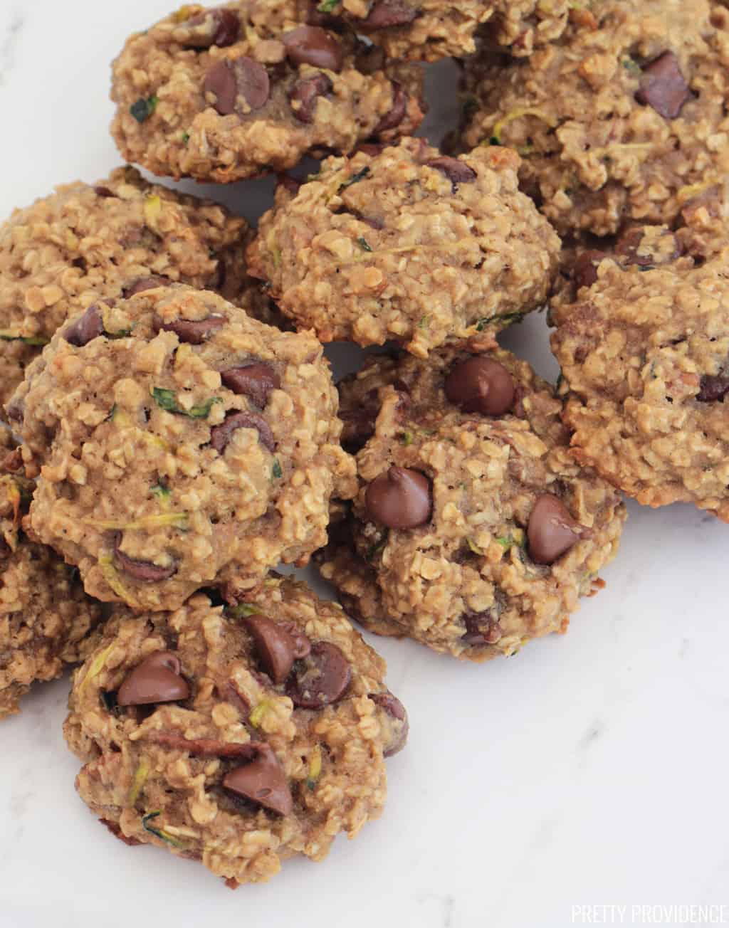 Zucchini breakfast cookies with oatmeal and chocolate chips on a white marble surface.