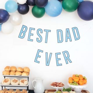 Father's Day breakfast table with breakfast sandwich ingredients, balloons and 'best dad ever' banner.