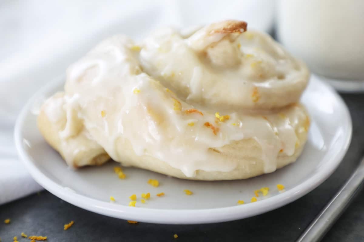 side view of a orange sweet roll on a white plate with milk in the background