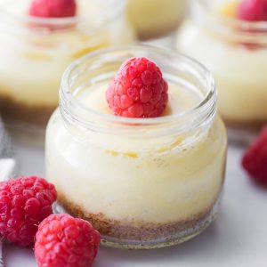 mini cheesecake in a small glass jar with raspberries to the side of it