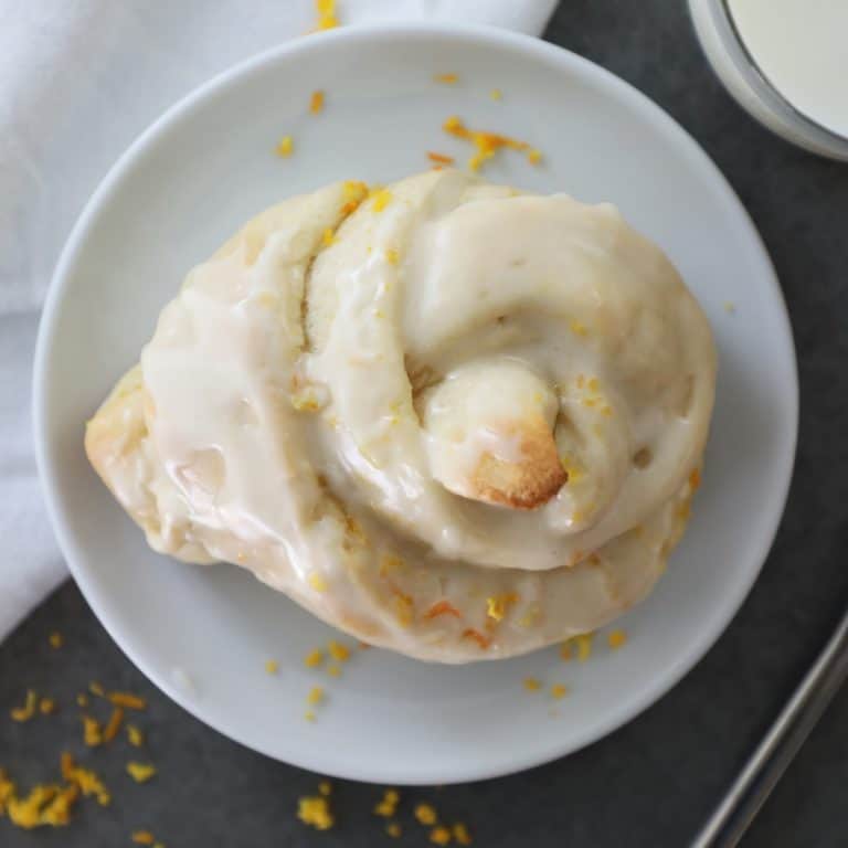 birds eye view of an orange roll on a white plate on a cement counter