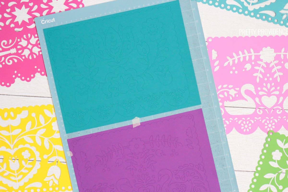 Teal and purple card stock on a blue Cricut LightGrip mat, papel picado pieces surrounding