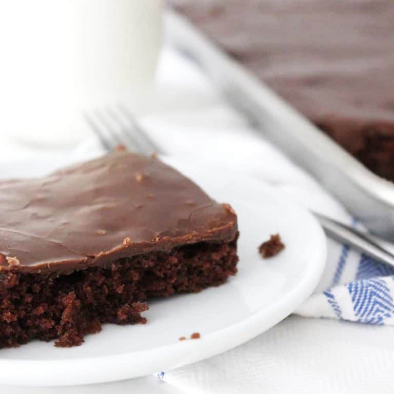 a slice of texas sheet cake on a white plate next to the full cake