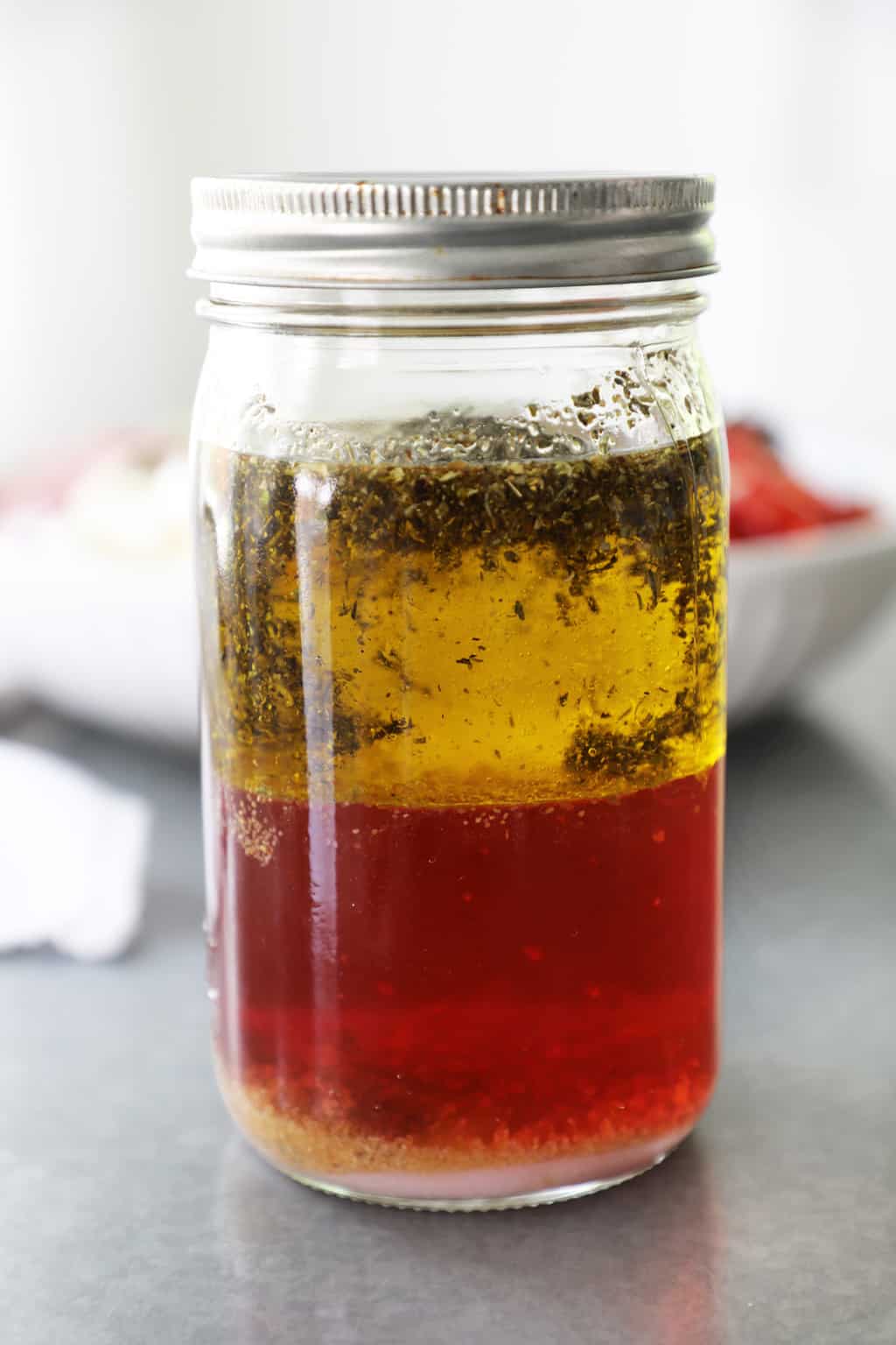 a mason jar with oil and vinegar and spices on a cement countertop