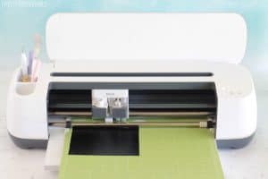 white Cricut maker machine cutting black vinyl on a green mat
