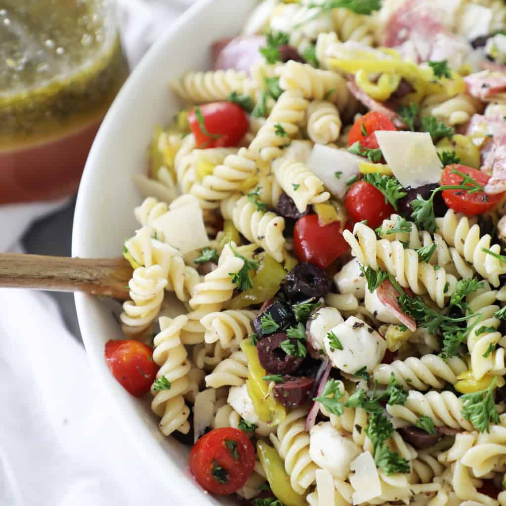 pasta salad in a white bowl next to a jar of dressing and a white napkin