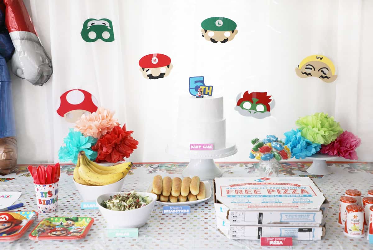 mario character masks hung on a white curtain in front of a party table