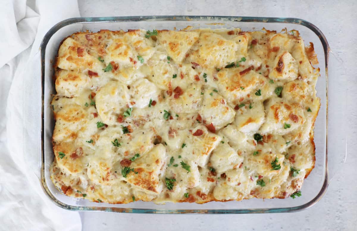 a full 9x13 dish of carbonara bake on a cement countertop garnished with fresh parsley