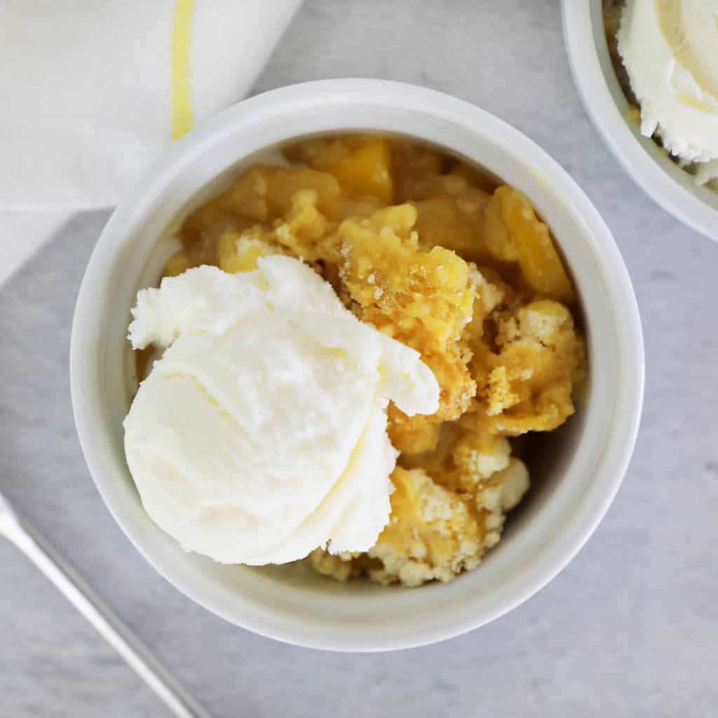 peach cobbler with vanilla ice cream in a small white dish on a cement counter