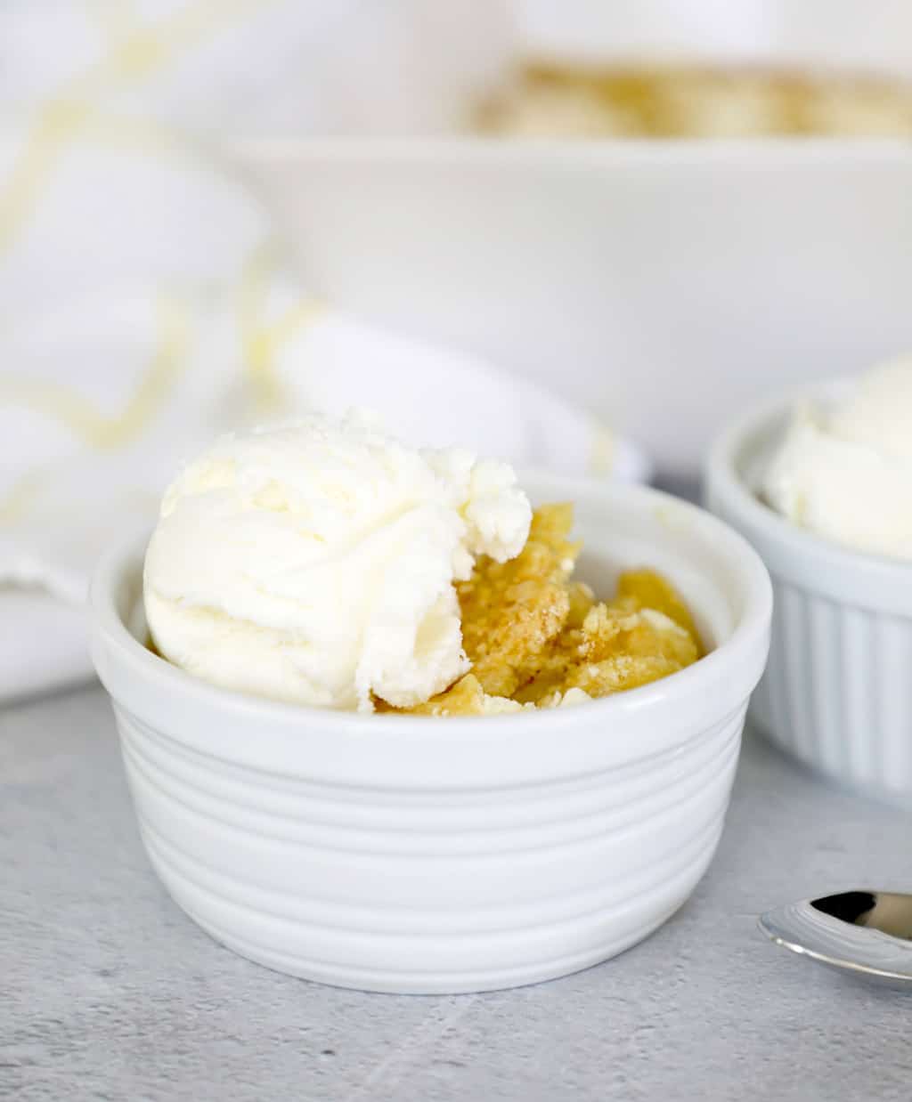 dish of peach cobbler in front of the white pan full of cobbler