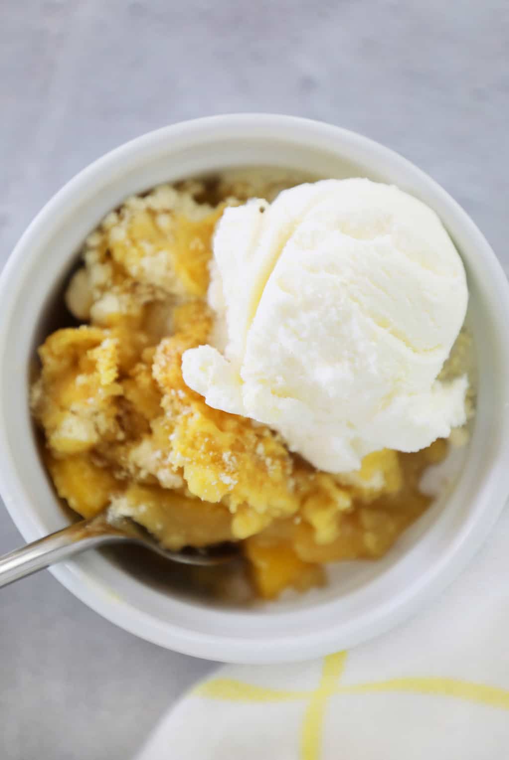 white dish with peach cobbler, ice cream, and a spoon sticking out