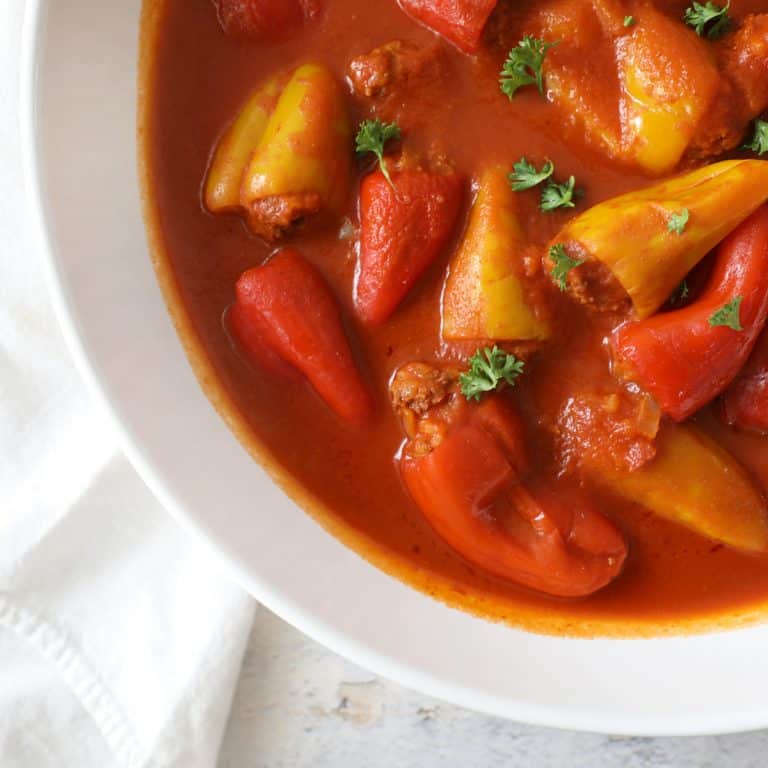 a corner of a large bowl of stuffed peppers in tomato sauce next to a white cloth napkin