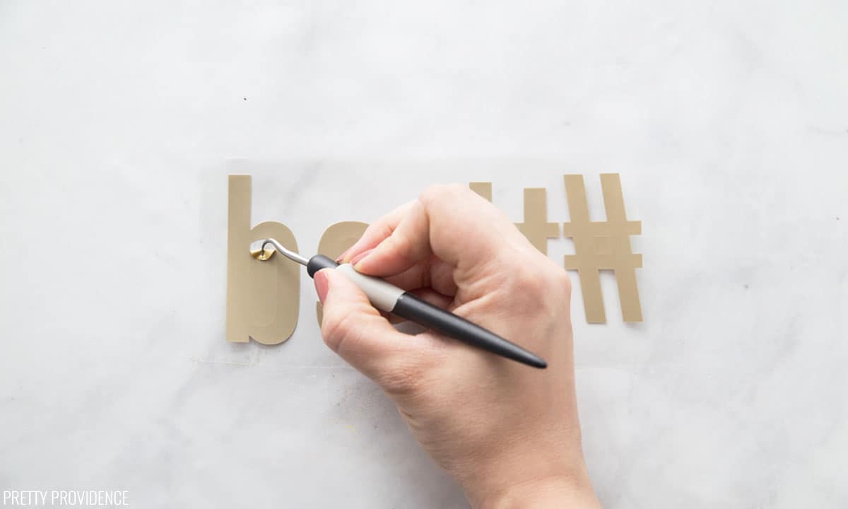 Gold Cricut iron-on vinyl being weeded with a small weeding tool.