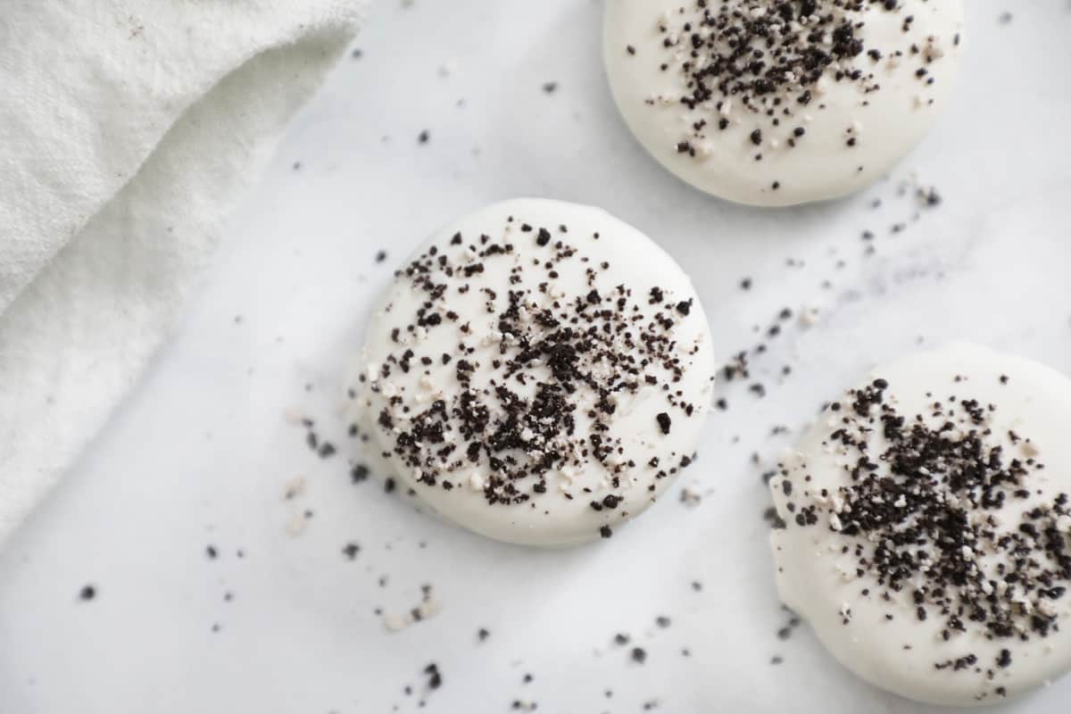 three white chocolate covered oreos surrounded by crumbs