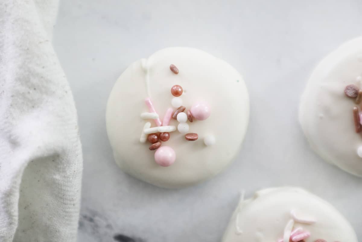 white chocolate covered oreo with pink colored sprinkles next to a white towel