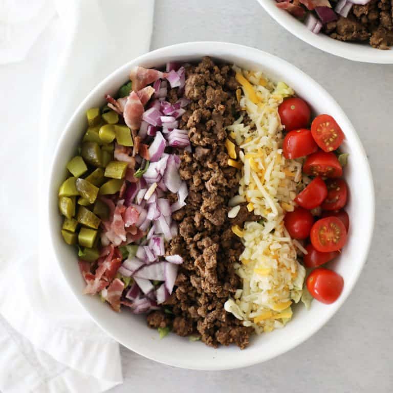 cheeseburger salad in a white bowl next to a white tea towel