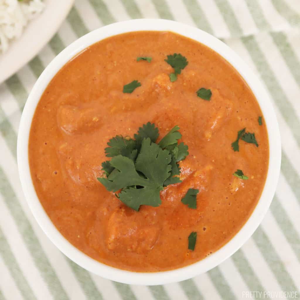 chicken tikka masala in a white bowl garnished with fresh greens and a white napkin