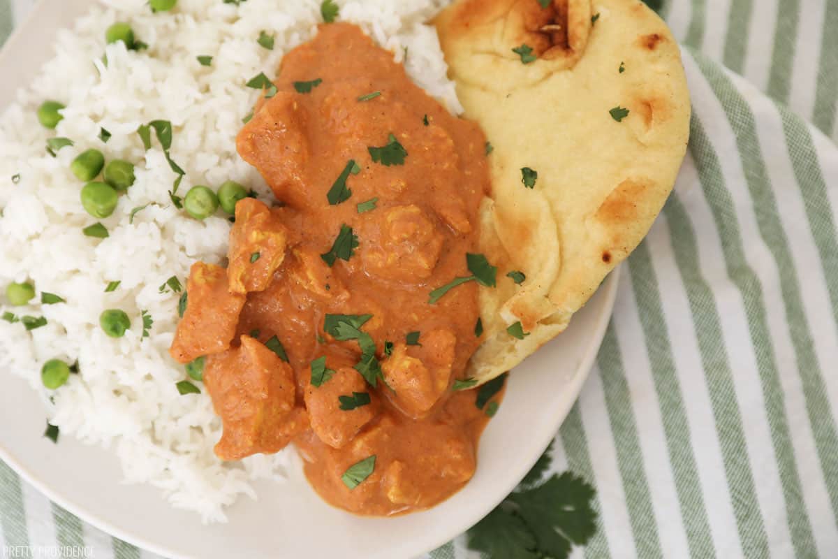 a plate of basmati rice and chicken tikka masala with naan, garnished with cilantro.