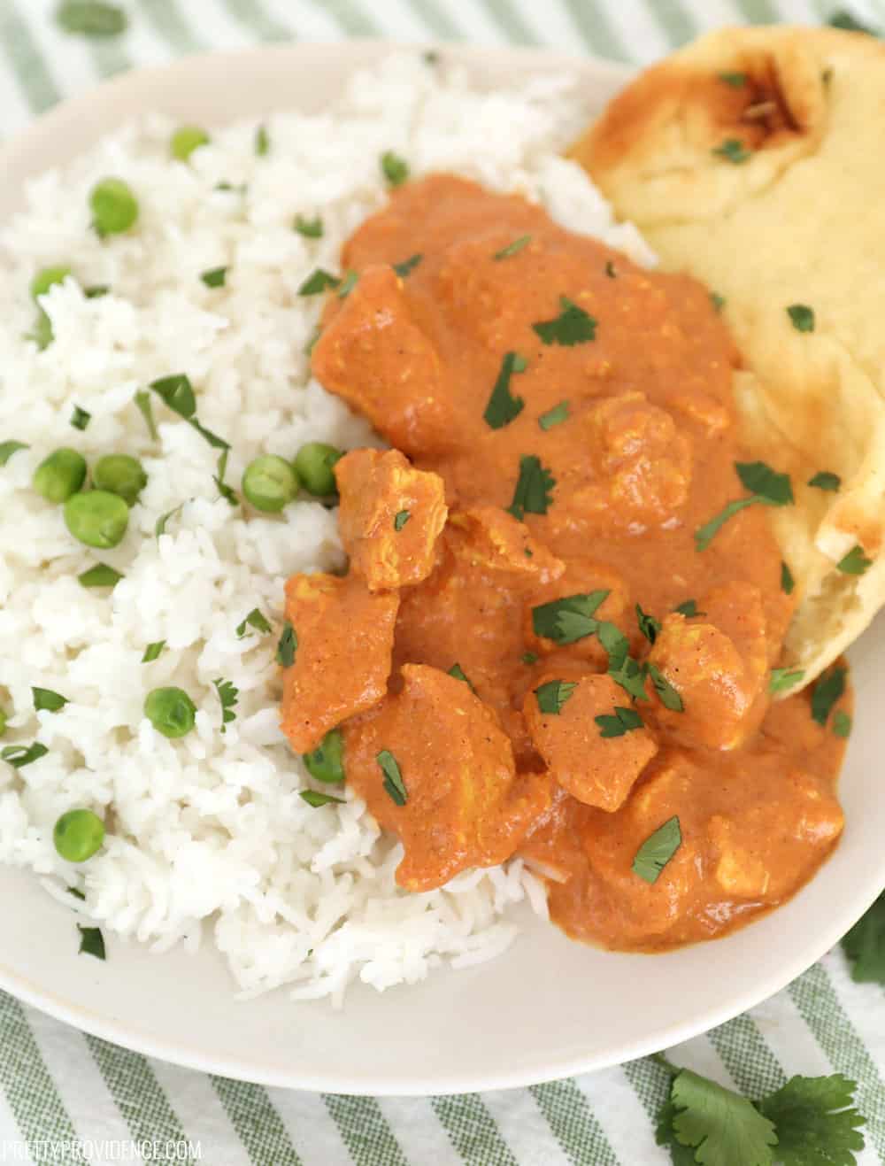 tikka masala in a white bowl with naan bread in the top right corner and rice in the bottom