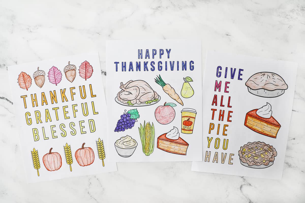 three different thanksgiving coloring pages colored on a granite countertop