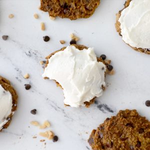 frosted pumpkin cookie with a bite taken out of it surrounded by cookies and walnuts and chocolate chips