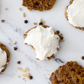 frosted pumpkin cookie with a bite taken out of it surrounded by cookies and walnuts and chocolate chips