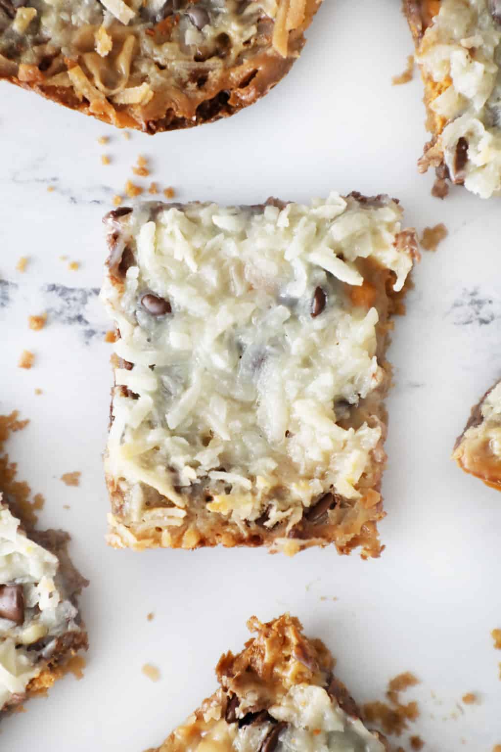 magic cookie bars on a white marble counter surrounded by crumbs