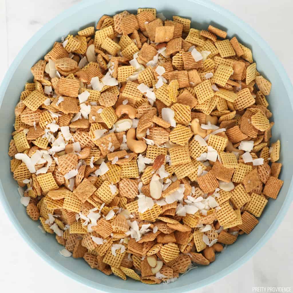 Sweet Chex mix dry ingredients in a large mixing bowl. Chex, Crispix and Golden Grahams cereals mixed with coconut flakes, sliced almonds and cashews.