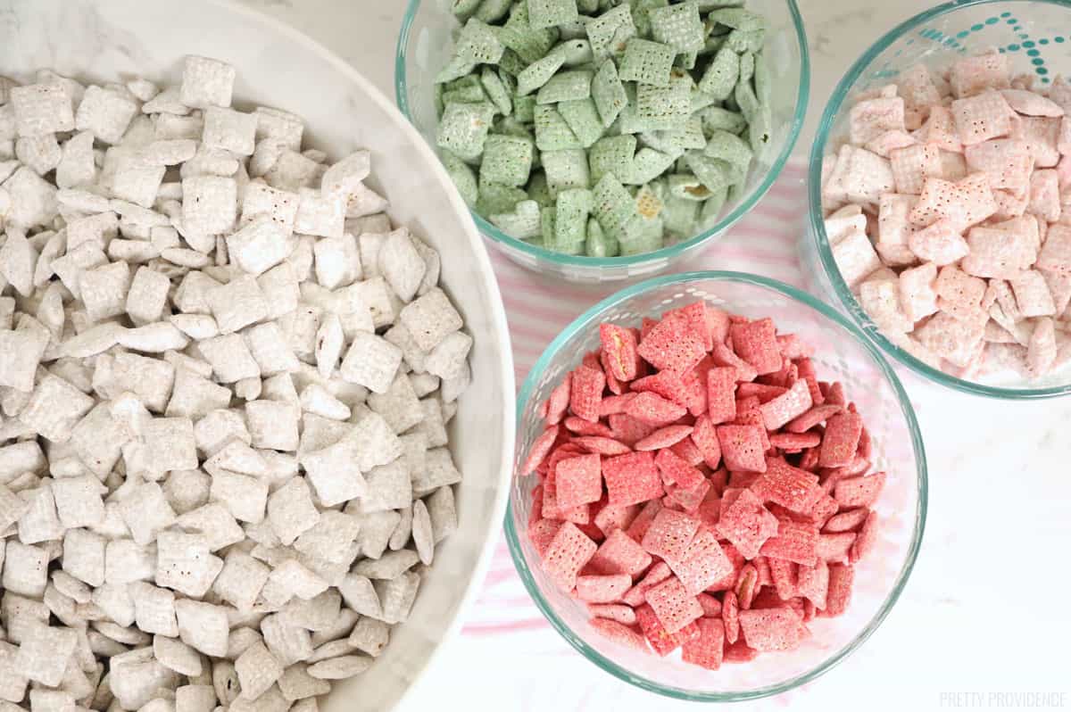 Chex cereal covered in red, pink and green candy coating and powdered sugar separated into bowls by color, muddy buddies AKA puppy chow