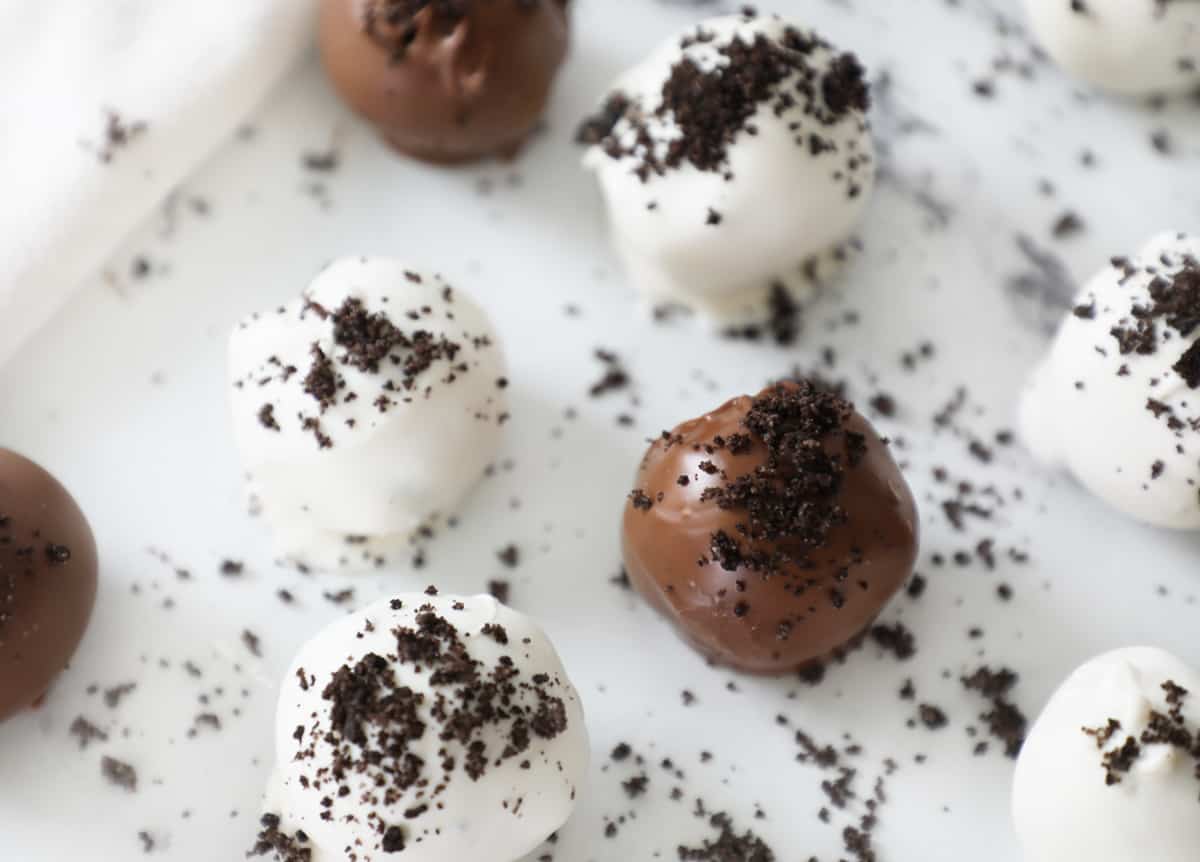 white and milk chocolate Oreo truffles surrounded by crumbs on a white counter