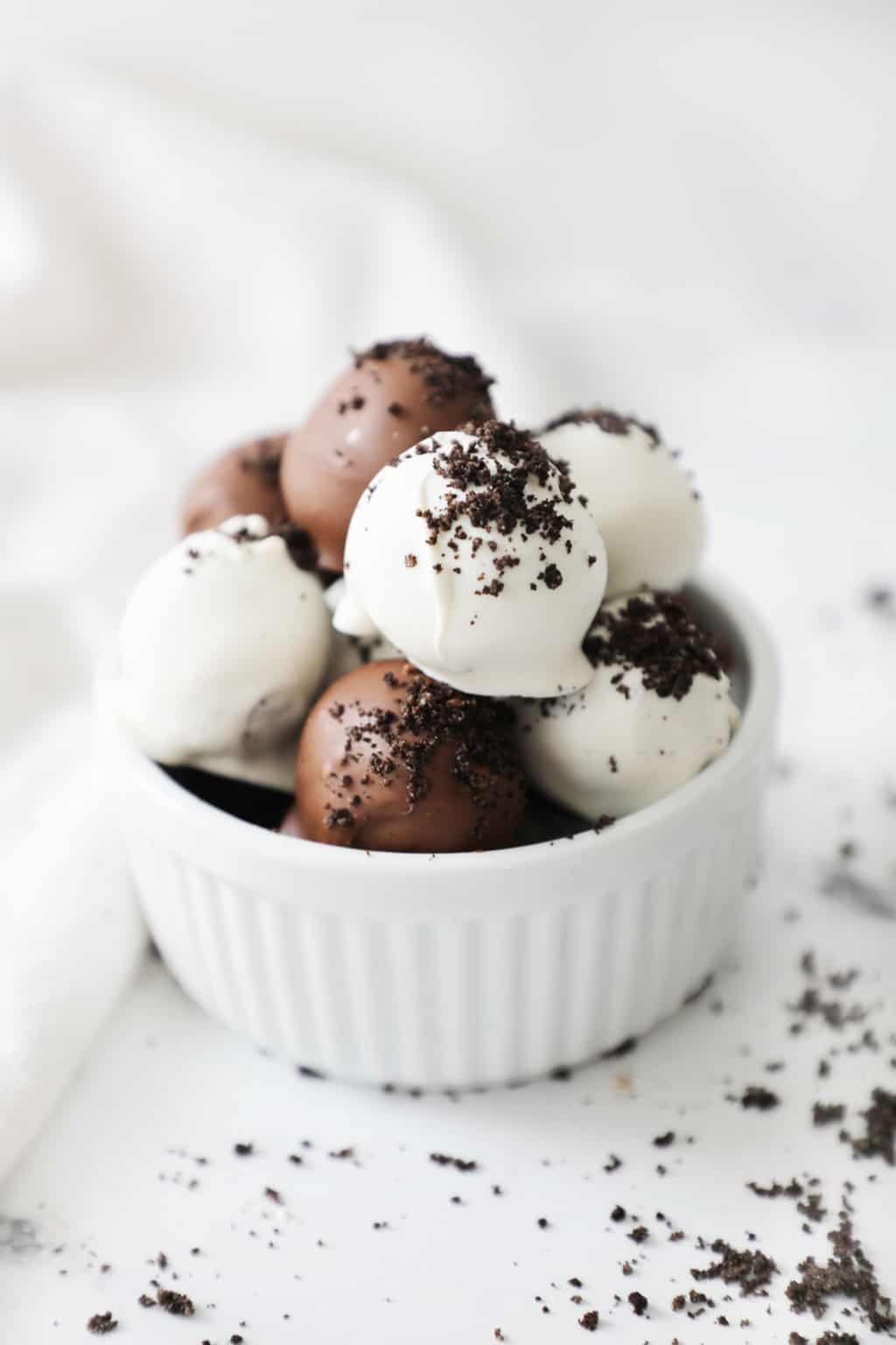 a white bowl overflowing with Oreo truffles next to a white linen napkin and some crumbs