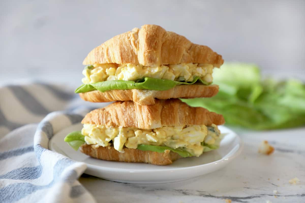 two stacked egg salad sandwiches on a small white plate