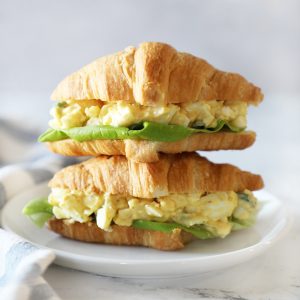 Two egg salad sandwiches stacked on a small white plate