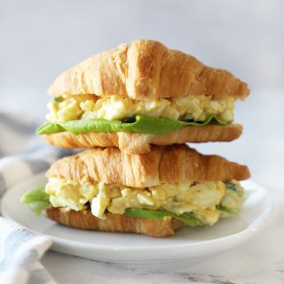 Two egg salad sandwiches stacked on a small white plate