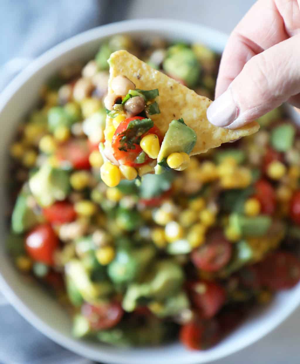 a chip with corn salsa held above the salsa bowl