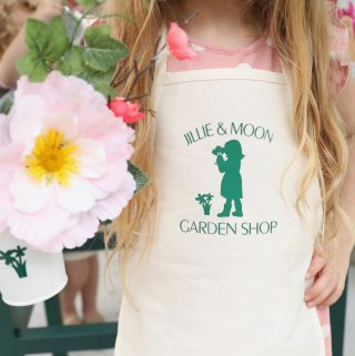 little girl holding flowers and wearing an apron with flowers and garden shop logo on it