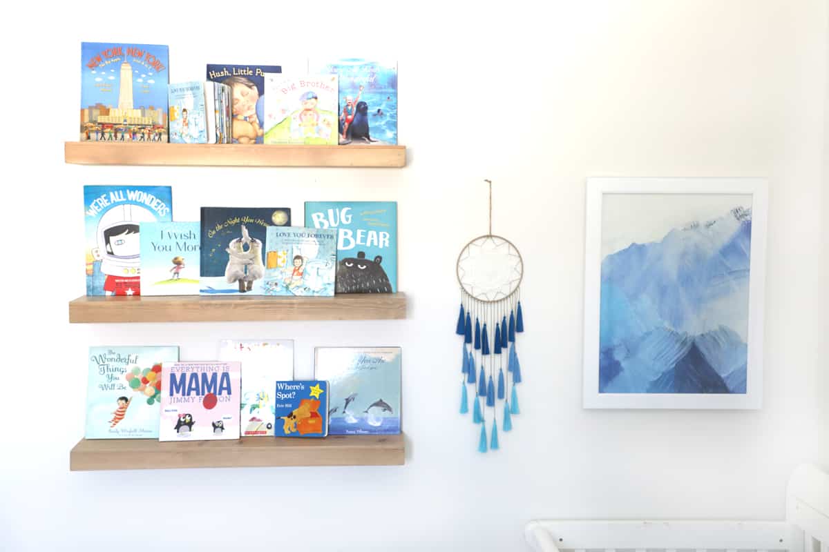 hanging shelves with blue books next to a dream catcher and a painting of blue mountains