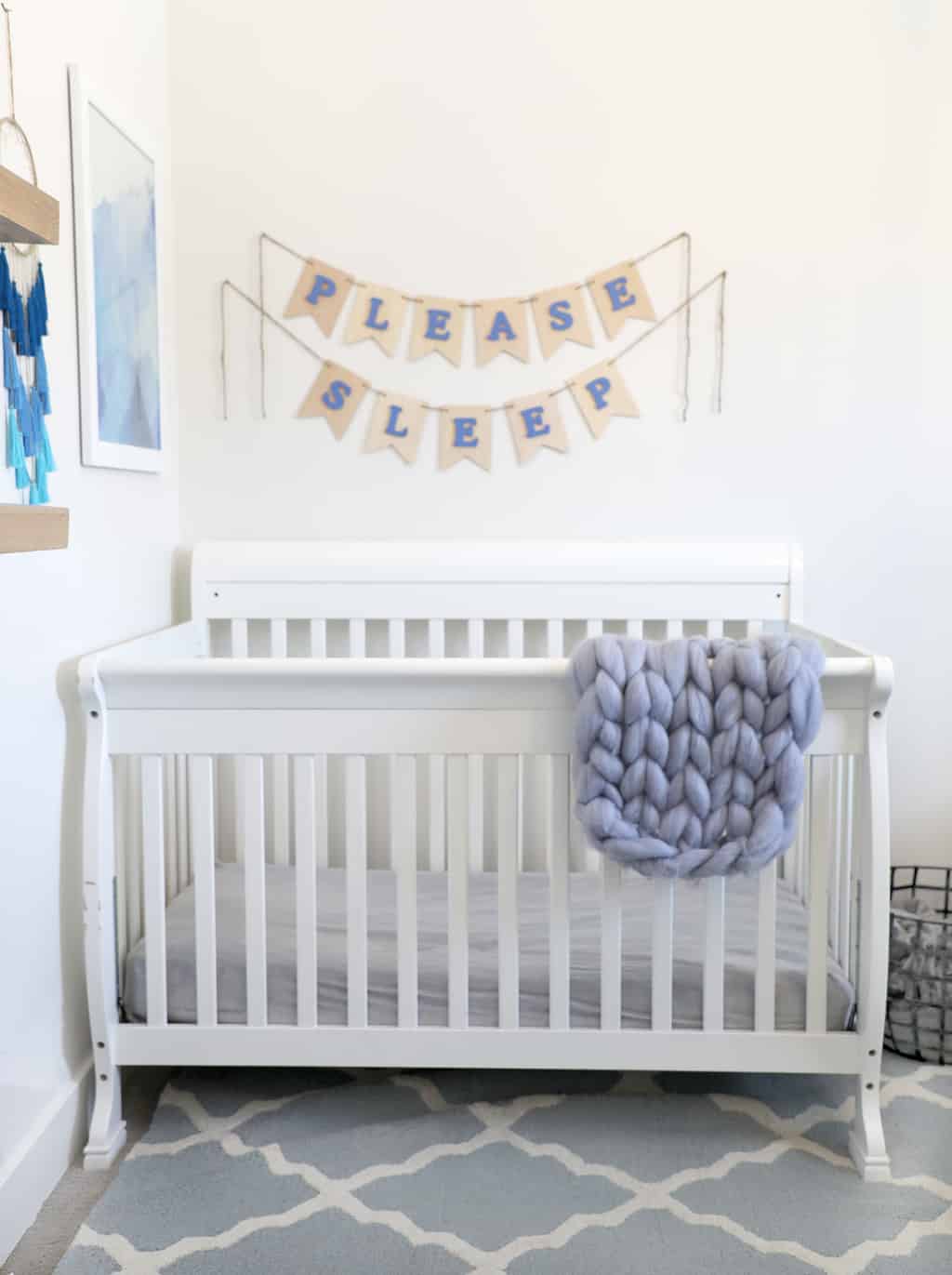 white crib against a white wall with blue accents and a "please sleep" banner