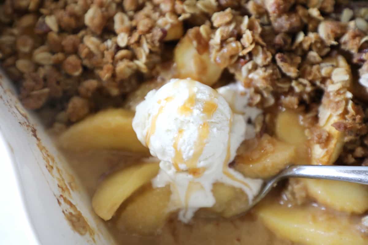 white pan of apple crisp with a spoon sticking out and ice cream on the corner