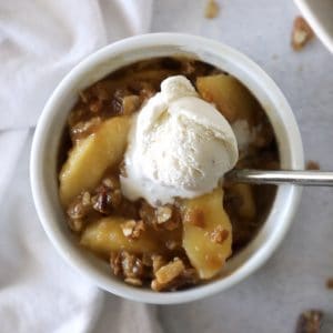 apple crisp in a white bowl with a small scoop of vanilla ice cream on top